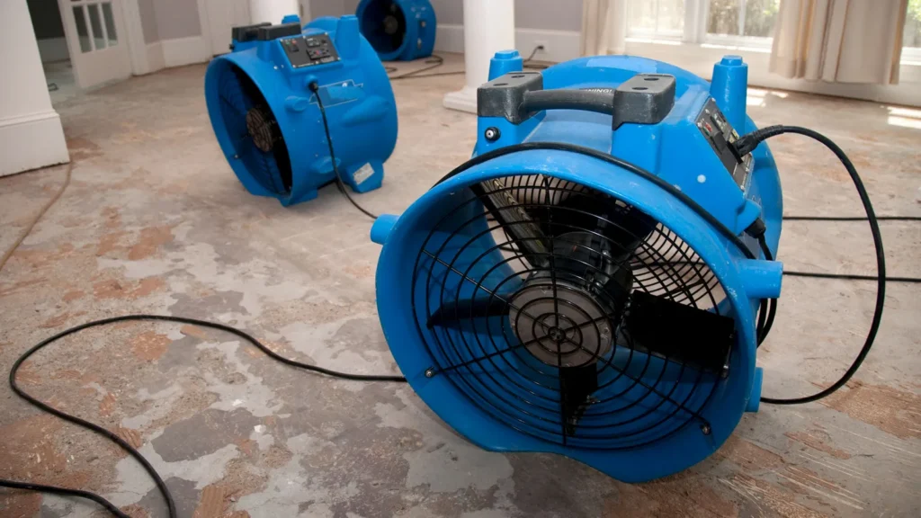 Blue air movers drying a water-damaged floor after a basement flood